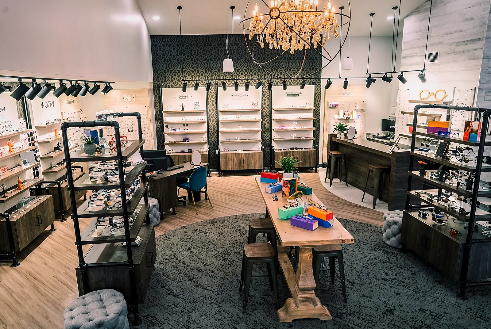 The Haywood Family Eye Care optical boutique &mdash; colorful designer frames on a warm wood table under a chandelier